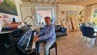 Peter Kusenbach in seinem Wohnzimmer in Kapsweyer. Klar. Piano, Harfe und Alphorn. Muss ja nicht alles gespielt werden, obwohl er es tut, aber schön anzuschauen sind die Instrumente allemal. Foto. rw. 