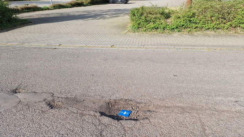 Ausschnitt der Schlagloch-Piste Friedrich-Ebert-Straße in BZA in Höhe des Schul-P-Platzes. Zum Größenvergleich haben wir mal eine herkömmliche P-Scheibe in das wohl größte Schlagloch vor Ort gelegt. Weitere Schlaglöcher gibt es zuhauf auf dem Weg weiter aufwärts zum benachbarten Hallenbad. Foto. rw. 