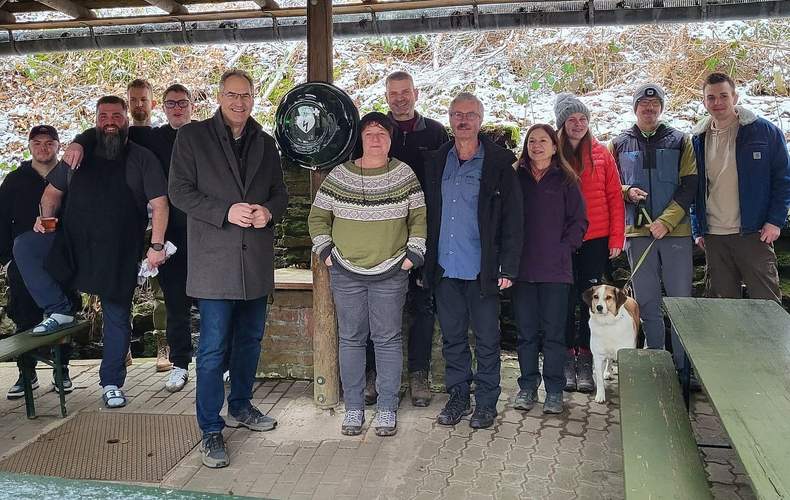 Landrat Dietmar Seefeldt (Fünfter von links) mit Engagierten des Wanderclubs Nello am AED-Gerät, das unter einem Unterstand an der Nello-Hütte befestigt und dadurch leicht zugänglich ist. Foto. KV. SÜW. Frei.